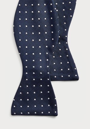 Navy bow tie made of textured fabric, featuring evenly spaced white polka dots. Classic shape with pointed ends and a slight sheen.