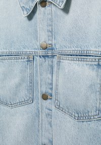 Veste en jean bleu clair vue de face montrant le col, les boutons en métal, les poches doubles sur la poitrine et les coutures détaillées.