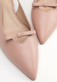 Ballerine in pelle rosa con punta affusolata, caratterizzate da un design con ritagli e un piccolo fiocco decorativo sulla parte superiore. Texture liscia e dettagli di cucitura minimi.