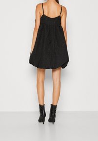 Svart, strukturerad klänning med figursydd överdel och flödande, utsvängd kjol. Har tunna axelband och rundad rygg. Bärs med svarta ankelstövlar.