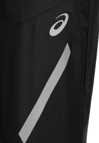 Tissu noir avec un logo Asics blanc et une bande réfléchissante diagonale sur le côté du vêtement de sport.