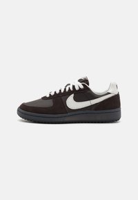 Nike tenisice s tamnosmeđim nubukom i kožom, bijelim detaljima i gumeni potplat s teksturiranim dizajnom, vezane bijelim vezicama.