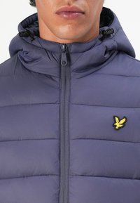 Navy puffer jacket with horizontal stitching, a high collar, and a zipper closure. Features a small yellow logo on the left chest area.