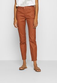 Rust-colored pants with a tailored fit, featuring a button closure, high waist, and smooth texture. Styled with a casual white top.