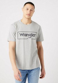 Gray cotton t-shirt with short sleeves and a round neck. Features a prominent black "Wrangler" logo on the front. Fitted design.