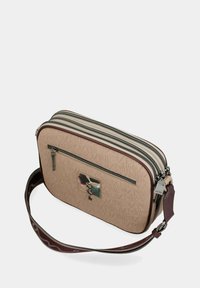 Beige strukturierte Umhängetasche mit zwei Reißverschlussfächern, vorderer Reißverschlusstasche, abstraktem Metall-Logo und verstellbarem burgunderrotem Gurt.