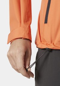 Oranje lange mouw jack met een ritszak, verstelbare zoomkoord en een gladde textuur. Draagt over donkere broeken.