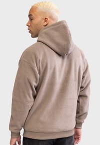 Polarowy hoodie w kolorze taupe, z dużym kapturem, ściągaczami przy rękawach i na dole. Tekstura wydaje się miękka i lekko puszysta.