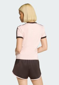 Różowy top z krótkim rękawem z brązowymi akcentami, zestawiony z brązowymi szortami. Miękka tkanina, elegancki design i kontrastujące wykończenia.