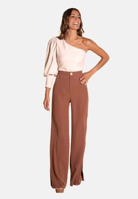 Top crema sin hombros con manga abullonada; pantalones de tiro alto y pernera ancha marrones con detalle de abertura en la parte delantera; modelo de pie, con las manos en las caderas.