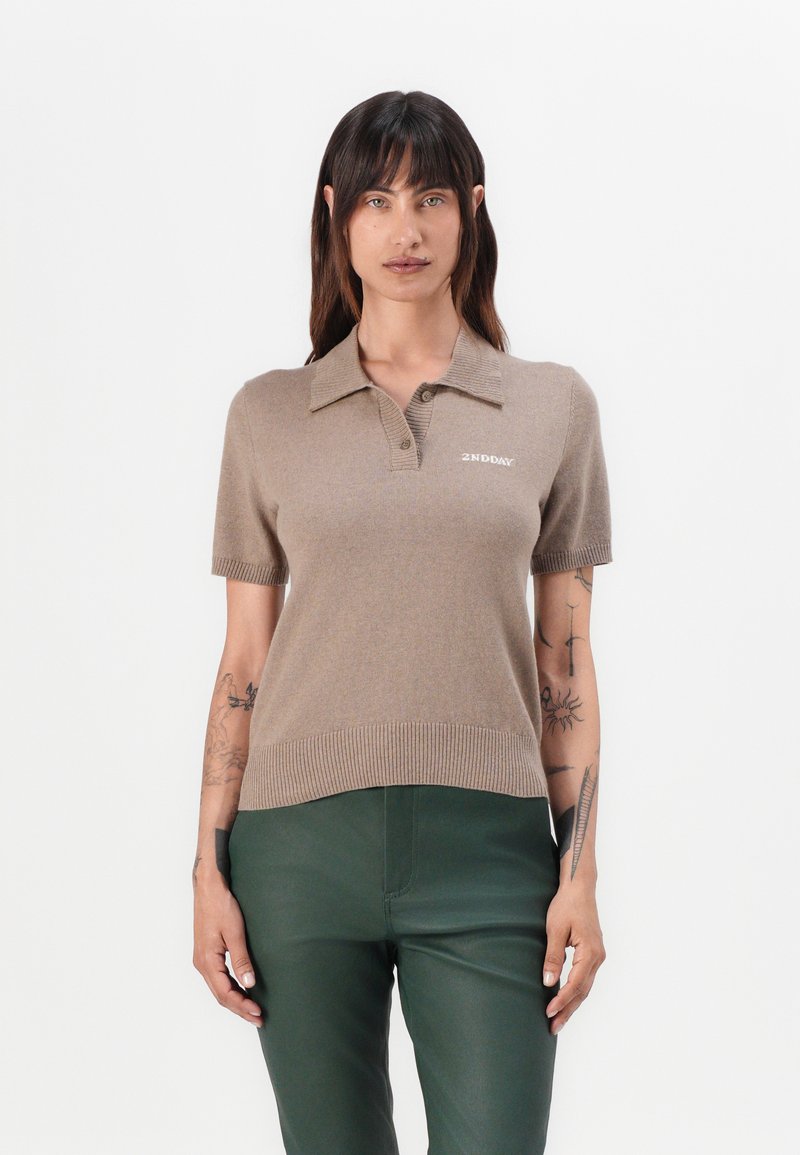 Kortermet beige polo genser med ribbestrikket kant, med krage og liten hvit "2ND DAY" logo på brystet. Myk strikket tekstur.