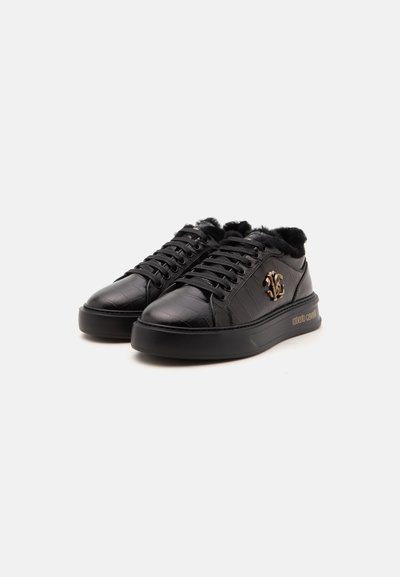 Paire de baskets basses en cuir noir avec doublure en fourrure, logo doré sur le côté et semelles épaisses noires sur fond clair.