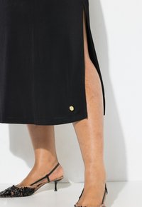 Musta hame, jossa on sivusaumaaukko, valmistettu sileästä kankaasta, ja helman kohdalla on pieni kultainen yksityiskohta. Mustat avokkaat, joissa on kukkakuviot.