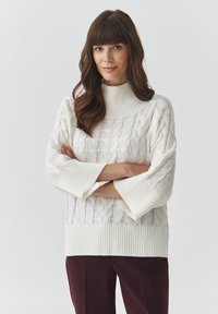 Maglione bianco a trama cable-knit con collo alto e maniche 3/4, caratterizzato da polsini e orlo a coste. Abbinato a pantaloni color bordeaux intenso.