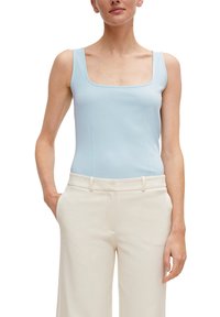 Ljusblå bodysuit med fyrkantig halsringning, tillverkad av slät textil. Matchad med högmidjade byxor i krämfärg, med en sömlös bälte.