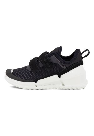 Baskets noires de sport avec tige en mesh, semelle en caoutchouc, deux sangles réglables et accents blancs. Design flexible pour faciliter les mouvements.