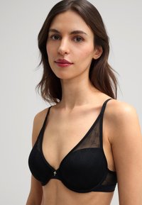 Zwarte beha met een gladde cupdesign, kantaccenten, verstelbare bandjes en een klein decoratief sieraad in het midden.