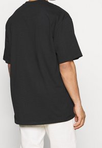 Černé bavlněné tričko s uvolněným střihem. Má krátké rukávy a kulatý výstřih. Bez viditelných log nebo vzorů. Jednoduchý a minimalistický design.