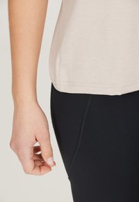 Beige kortärmad skjorta med en mjuk textur, bärs över svarta leggings. Skjortan har en böjd fåll och subtila sömnadsdetaljer.