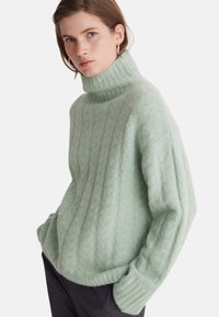 Hellgrüner Strickpullover mit hohem, geripptem Kragen, strukturierten Mustern und gerippten Bündchen. Lockerer Schnitt mit seitlichen Taschen.