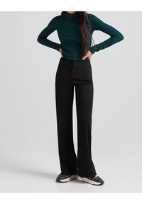 Cuello de tortuga verde acanalado combinado con pantalones de pierna ancha negros de cintura alta. La modelo lleva zapatillas negras; texturas suaves y diseño ajustado visibles.