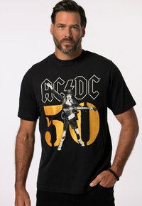 Sort bomulds t-shirt med AC/DC grafik. Designet inkluderer en vintage figur der holder en guitar, med fed gul tekst "50" og logo.