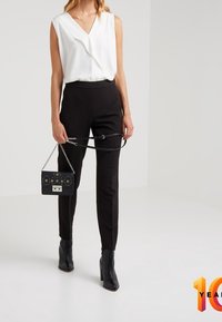White sleeveless blouse with a V-neck, black tailored pants, and ankle-length black heeled boots. Holding a small black handbag with decorative accents.