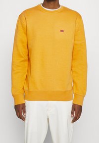 Gele sweatshirt van een katoenmix, met een ronde hals, geribbelde boorden en een klein rood Levi's-logo op de borst. Soepele textuur.