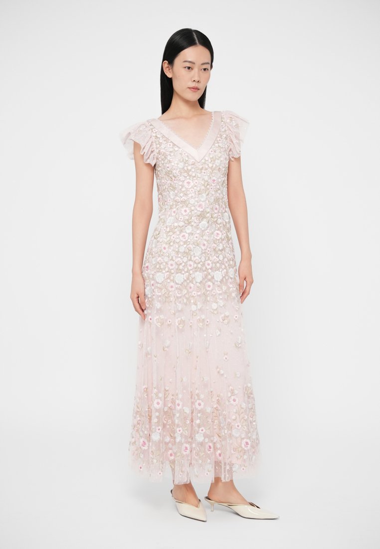 Robe longue rose avec broderies florales, tissu transparent et manches courtes à volants. Décolleté en V et ourlet fluide avec des détails superposés.