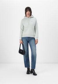 Hellgrüner Hoodie mit Fronttasche, kombiniert mit blauen Jeans im geraden Schnitt und schwarzen Knöchelboots. Schwarze Handtasche mit Logodetail.