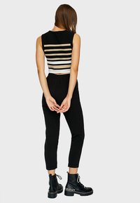 Top court noir avec des rayures blanches et beiges, associé à un pantalon noir fuselé et des bottes à talons aiguilles à lacets avec "RIGHT" imprimé sur le côté.