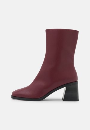 Bottes cheville bordeaux avec une surface lisse et texturée, bout pointu, et un talon carré avec un design rainuré.