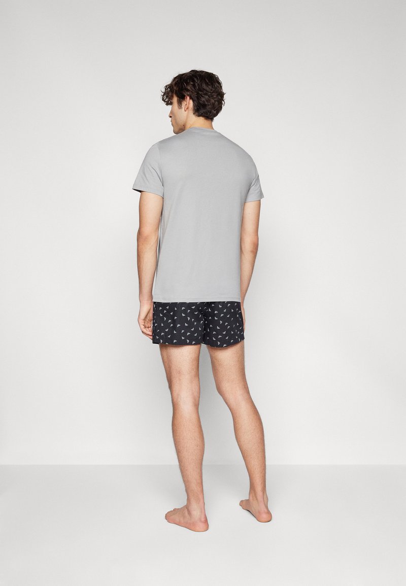 Graues kurzärmliges T-Shirt und schwarze gemusterte Shorts, von hinten betrachtet. Das T-Shirt besteht aus weichem Material; die Shorts haben ein kleines Dreiecksmuster.
