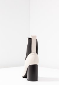 Černé a krémové kotníkové boty s vysokým blokovým podpatkem, s texturovaným svrškem a zadním poutkem pro snadné nazouvání.