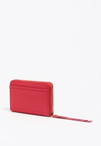 Cartera roja con cremallera y textura lisa, que cuenta con un compartimento para tarjetas en la parte trasera y un acento de borla decorativa. Herrajes de cremallera en tono dorado.