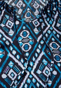 Gemusterter Stoff mit einem blau-weißen geometrischen Design auf einem dunkelblauen Hintergrund, der eine fließende und strukturierte Erscheinung aufweist.