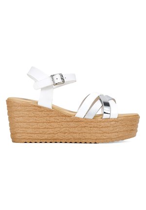 Sandales compensées blanches avec une semelle en liège texturée, ornées d'accents argentés métalliques et d'une bride de cheville ajustable, au design à brides croisées.