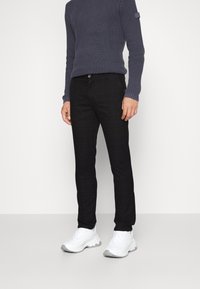 Granatowy prążkowany sweter, czarne, wąskie spodnie w kratę oraz białe trampki z teksturowaną podeszwą. Spodnie mają kieszenie i zapięcie na guziki.