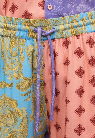 Patchworková textília s modrými a broskyňovými časťami, zlatými paisley a červenými kvetinovými vzormi a fialovým sťahovacím šnúrkou previazanou v páse.