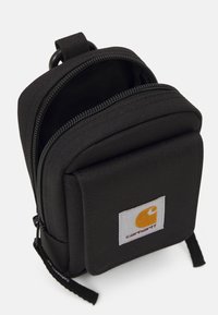 Saco mini de tecido preto com um fecho de correr de duas vias, bolso frontal com apliques e o logótipo da Carhartt. Apresenta uma alça superior robusta e uma superfície texturizada.