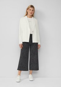 Blazer blanc ajusté avec un bouton unique, porté sur un t-shirt blanc. Assorti avec un pantalon large à motif noir et des baskets blanches.