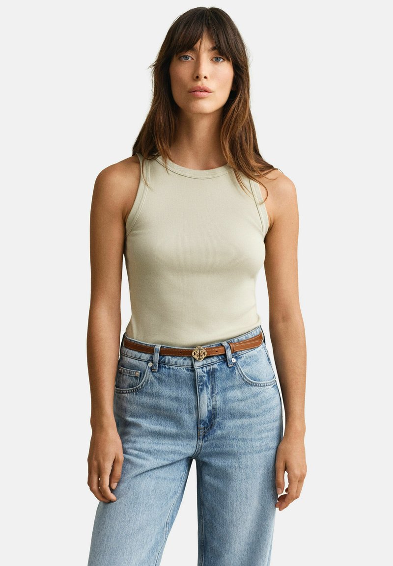 Mujer con un top sin mangas beige de canalé, jeans azul claro de cintura alta y un cinturón marrón con una hebilla decorativa dorada.