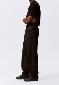 Zwarte denim wijde pijpen jeans met een hoge taille, voorzien van contrasterende stiksels en voorzakken, gecombineerd met een aangesloten zwarte t-shirt en zwarte schoenen.