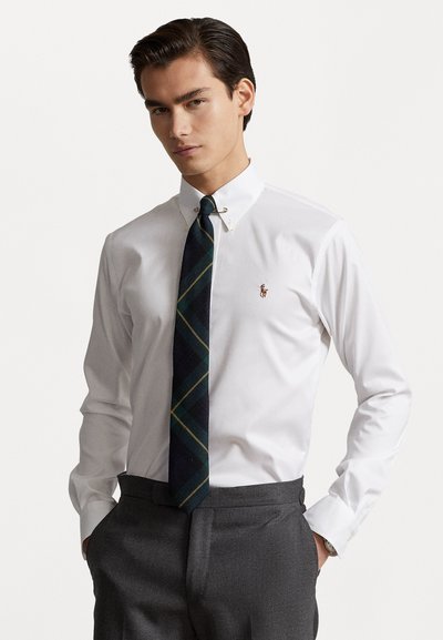 Witte overhemden met button-down kraag, met een klein logo op de borst, gecombineerd met een donker geruite stropdas en grijze broek.