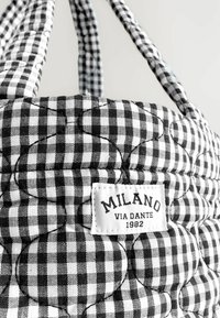 Quilted black and white checkered fabric tote bag with flower stitching and a white label reading "MILANO VIA DANTE 1982."