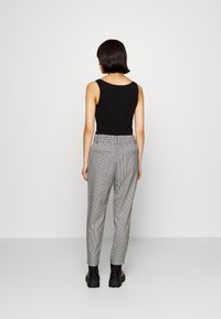 Svart ärmlös topp i kombination med grå och vit rutmönstrad byxor med hög midja och elastisk midjeband. Svarta ankboots.