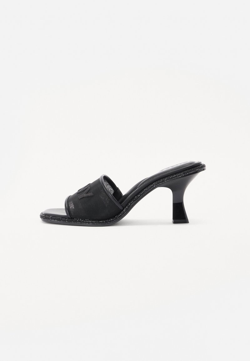 Mule noire à bout ouvert avec talon moyen incurvé et bride texturée avec logo embossé subtil.
