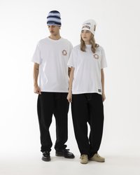 Weiße T-Shirts mit kleinen Logo-Akzenten, kombiniert mit schwarzen, weiten Hosen. Einer trägt eine blau-gestreifte Mütze; der andere hat eine weiße Mütze mit Text.