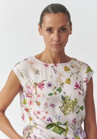 Kvetinová potlač na vrchu z ľahkej, jemnej tkaniny; má okrúhly výstrih a krátke rukávy; farby vrátane ružovej, zelenej a fialovej.