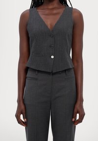 Grå randig väst med V-ringning, som har två framknappar och en figurnära silhuett, kompletterad med matchande skräddarsydda byxor.